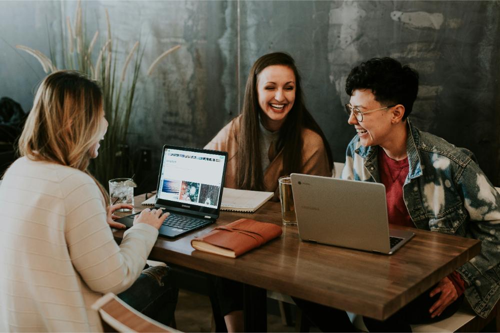 Group of professional ladies laughing together during meeting while working on their laptops